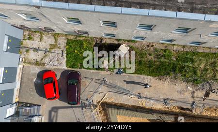 Vue aérienne d'un chantier de construction à côté d'un bâtiment avec voitures stationnées et ouvriers. Banque D'Images