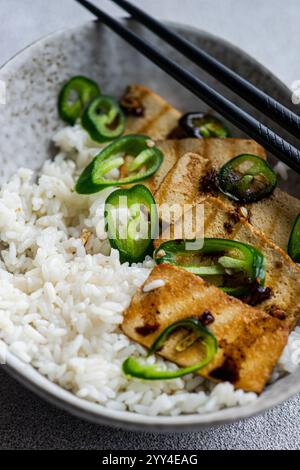 De haut en haut de tranches de tofu grillé assaisonnées et servies avec du riz blanc et des rondelles de poivre vert épicé, magnifiquement présentées avec des baguettes au repos Banque D'Images