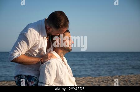 Un jeune couple gay partage un moment tendre sur la plage un partenaire embrasse le front de l'autre alors qu'ils apprécient le paysage paisible du bord de mer, célébrant Banque D'Images