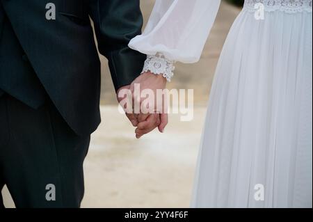 Un gros plan d'un couple se tenant par la main, mettant en évidence les détails de la tenue de mariage la robe en dentelle de la mariée et le costume du marié symbolisent l'amour, l'unité, et a TI Banque D'Images