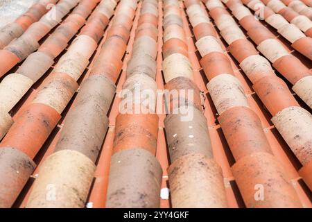 Vue détaillée des tuiles de toit classiques en argile sous la lumière du soleil. Les tons terreux et la texture soulignent la durabilité et l'attrait esthétique du roo traditionnel Banque D'Images