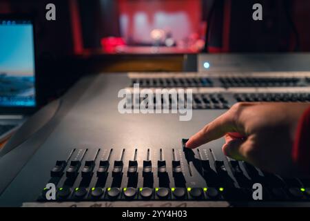 La main d'une personne règle précisément les commandes sur une table d'harmonie dans un studio faiblement éclairé. L'arrière-plan flou fait allusion à une scène, capturant une atmosphère Banque D'Images