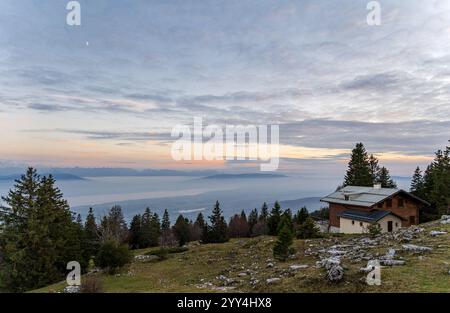 Vue captivante sur Genève et le lac Léman depuis le Jura suisse, avec un chalet rustique, une forêt luxuriante et un ciel serein aux couleurs pastel à l'aube, embod Banque D'Images