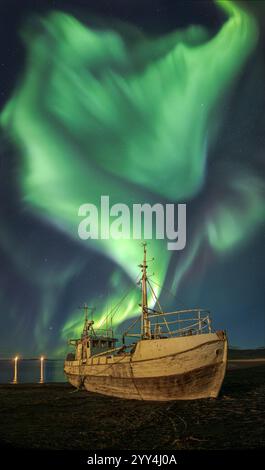 Un spectacle époustouflant des aurores boréales danse au-dessus d'un bateau abandonné sur une côte islandaise, créant une scène nocturne surréaliste et fascinante riche en esprit Banque D'Images