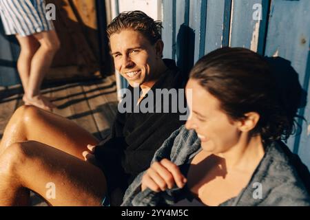 Portrait à angle élevé de jeune homme souriant portant un peignoir tout en étant assis avec une amie au jour ensoleillé Banque D'Images