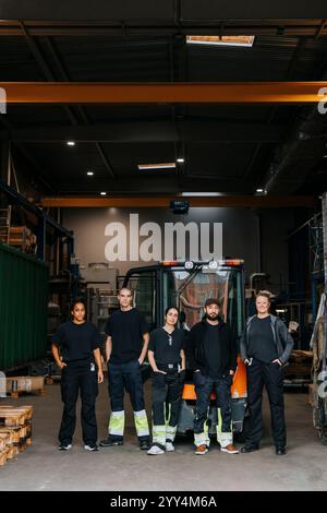 Portrait d'ouvriers d'entrepôt multiraciaux hommes et femmes debout avec les mains dans les poches devant un chariot élévateur Banque D'Images