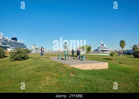 Civitavecchia, Italie - 19 décembre 2024 : Statue d'officier de marine dans le parc riverain et bateaux de croisière amarrés entourés de touristes capturant la scen Banque D'Images