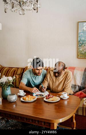Infirmier aidant homme senior à résoudre des mots croisés dans le journal à la maison Banque D'Images