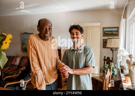 Portrait d'un vieil homme souriant debout avec un infirmier masculin dans le salon à la maison Banque D'Images