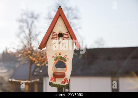 Nichoir en bois orné de fleurs colorées et de champignons fantaisistes, niché dans un jardin serein pendant la saison hivernale tranquille Banque D'Images