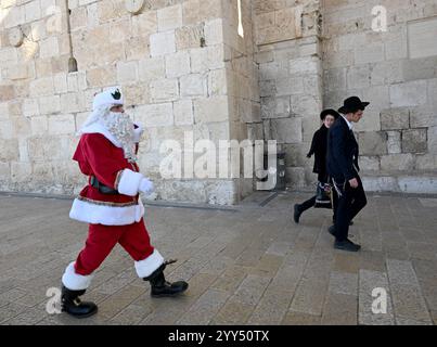 Vieille ville Jérusalem, Israël. 19 décembre 2024. Des hommes juifs orthodoxes marchent près du chrétien palestinien Issa Kassissieh, habillé en Père Noël, devant la porte de Jaffa dans la vieille ville de Jérusalem, le jeudi 19 décembre 2024. Photo de Debbie Hill/ crédit : UPI/Alamy Live News Banque D'Images