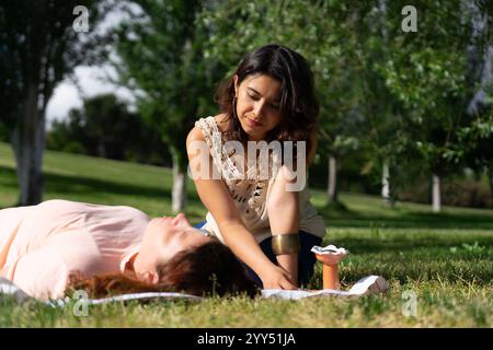 Thérapeute effectuant un traitement de guérison reiki sur un patient allongé sur une couverture sur l'herbe dans un parc Banque D'Images