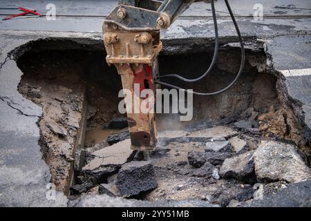 Ouvrier de construction de route avec des machines réparer énorme gouffre sur la surface occupée de la route asphaltée sur laquelle les voitures roulent. Situation accidentelle dans une rue de ville Banque D'Images