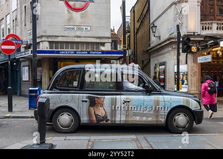 Londres, Royaume-Uni - 4 décembre 2024 : un taxi avec de la publicité attend un feu vert près de l'entrée de la station de métro Leicester Square. PEOP Banque D'Images