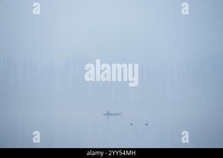 Un batelier cachemirien ramène son bateau à travers le célèbre lac Dal lors d'un matin d'hiver froid et brumeux à Srinagar. La vallée du Cachemire s'enroule actuellement dans des conditions de froid intense alors que la température minimale a chuté de plusieurs degrés en dessous du point de congélation. La capitale de la région, Srinagar, enregistre la nuit la plus froide de la saison à moins 6 degrés Celsius (21,2 degrés Fahrenheit), une fine couche de brouillard également observée dans de nombreuses parties de la vallée. Le bureau météorologique local a prédit un temps principalement sec jusqu'en décembre 26 avec une possibilité de chutes de neige légères dans les tronçons plus élevés de la région résistante de l'Himalaya Banque D'Images