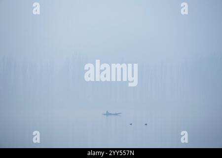 Un batelier cachemirien ramène son bateau à travers le célèbre lac Dal lors d'un matin d'hiver froid et brumeux à Srinagar. La vallée du Cachemire s'enroule actuellement dans des conditions de froid intense alors que la température minimale a chuté de plusieurs degrés en dessous du point de congélation. La capitale de la région, Srinagar, enregistre la nuit la plus froide de la saison à moins 6 degrés Celsius (21,2 degrés Fahrenheit), une fine couche de brouillard également observée dans de nombreuses parties de la vallée. Le bureau météorologique local a prédit un temps principalement sec jusqu'en décembre 26 avec une possibilité de chutes de neige légères dans les tronçons plus élevés de la région résistante de l'Himalaya Banque D'Images