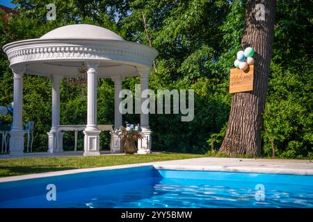 Configuration de décoration de luxe près de la piscine pour la célébration d'événements dans la terrasse arrière avec piliers en plâtre, avec table, fleurs, ballons et table de bienvenue Banque D'Images