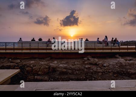 Les gens appréciant une vue sur le coucher du soleil depuis la promenade côtière près du château de Paphos, Chypre Banque D'Images