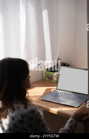 Concentrée jeune étudiante féminine engagée dans la recherche académique avec un ordinateur portable blanc vierge, écrivant des notes et étudiant en ligne. Banque D'Images