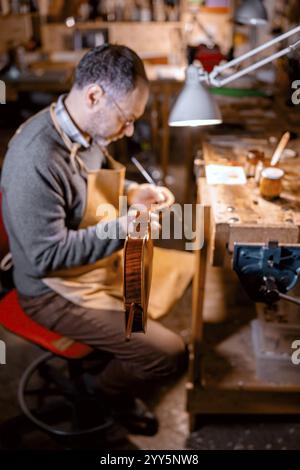 Luthier italien restaurant un violon dans un atelier, en utilisant des outils spécialisés sous la lumière chaude de la lampe, soulignant le dévouement et la précision dans l'artisanat str Banque D'Images