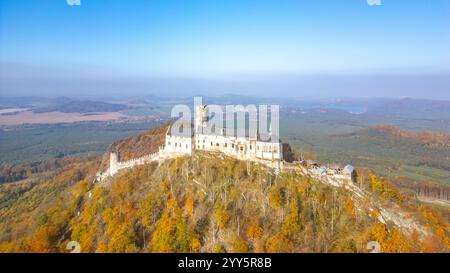 Le château médiéval de Bezdez se dresse majestueusement au sommet d'une colline, entouré d'un feuillage d'automne vibrant, mettant en valeur son importance historique sur fond d'arbres colorés et de collines lointaines. Banque D'Images