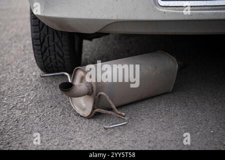 Échappement de voiture, silencieux tombé sur le sol dans la route de circulation, laissé derrière la voiture en arrière-plan. Chasis rouillé d'une voiture. Tuyau d'échappement endommagé. Banque D'Images