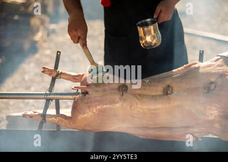 Un jeune cochon de lait sur une brochette. Porc rôti entier sur une broche en acier rotative avec feu et fumée. Grill traditionnel de Serbie, dans les Balkans, campagne Banque D'Images