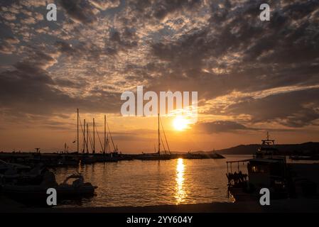 Belle scène de coucher de soleil sur le port dans un petit village de pêcheurs en mer à Nea Skioni, Grèce. Marina grecque avec sillhouetes de bateaux stationnés et yachts Banque D'Images