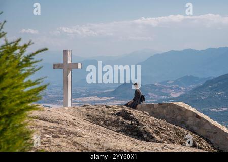 Mystérieux suspendu au-dessus des rochers monastères de Météores, Grèce. Fille assise à côté de la grande croix blanche, près du monastère de la Sainte Trinité. Kalambaka ville Banque D'Images