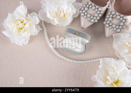 Une paire de chaussures chics avec une décoration de perles, des fleurs blanches, une boîte avec des anneaux, des perles de perles sur un fond beige. vue de dessus. Le concept du mariage. Banque D'Images