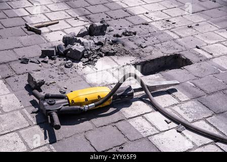 Une pierre a été enlevée d'un passage pour piétons avec une perceuse à percussion rotative électrique. Gros plan. Zone de construction ou travaux routiers sur la rue de la ville. Banque D'Images