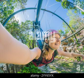 Femme en casque volant sur une tyrolienne au-dessus d'un parc tropical luxuriant. Aventure palpitante entourée par la nature, parfait pour l'éco-tourisme et l'adrénaline Banque D'Images