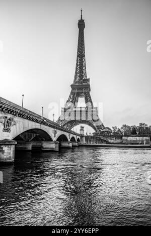 La Tour Eiffel se dresse majestueusement au-dessus de la Seine à l'aube, projetant un reflet époustouflant. La lumière matinale met en valeur la beauté de ce monument emblématique de Paris, offrant une vue sereine. Banque D'Images