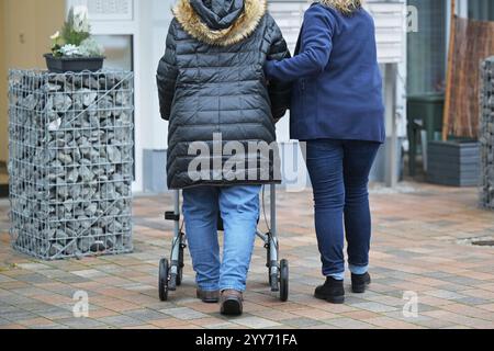 19 décembre 2024, Brandebourg, Werder (Havel) : une travailleuse de soins aide une personne âgée ayant besoin de soins, qui tient un déambulateur, sur le chemin de son domicile. Image symbolique de l'augmentation de la contribution aux soins de longue durée, le Bundesrat discutera, le vendredi 20 décembre 2024, entre autres, de l'augmentation de la contribution aux soins de longue durée. Le Gouvernement fédéral a déjà décidé d'augmenter le taux de cotisation à l'assurance sociale pour soins de longue durée. Photo : Michael Bahlo/dpa Banque D'Images