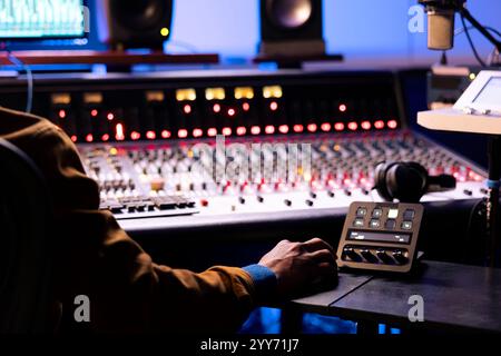 Expert afro-américain travaillant au panel de mixage en studio d'enregistrement. Utilisation de la table d'harmonie du pupitre de commande et de l'interface logicielle audio numérique sur pc, faders motorisés et mélangeurs pour éditer les pistes. Banque D'Images