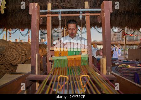 Un artisan arabe travaillant sur le tissage traditionnel du métier à tisser en bois avec des fils colorés lors du 14ème festival de boutre traditionnel Katara, Doha, Qatar Banque D'Images