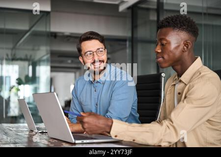 Deux employés masculins occupés et heureux utilisant des ordinateurs portables travaillant au bureau. Banque D'Images