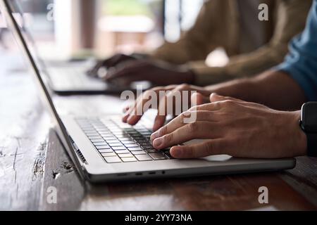 Gros plan photo de mains masculines tapant sur un ordinateur portable assis au bureau. Banque D'Images