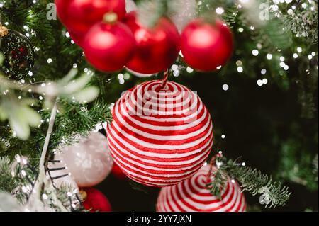 Une boule rayée rouge et blanche est suspendue à un arbre de Noël. Il y a aussi d'autres boules rouges et blanches sur l'arbre Banque D'Images