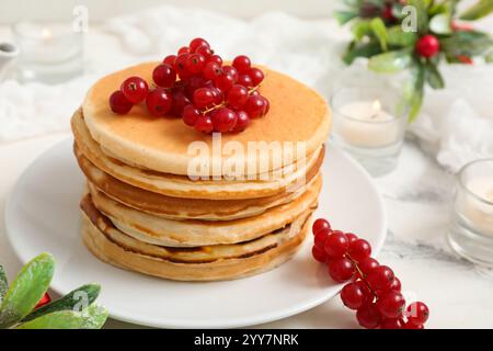 Assiette de crêpes sucrées avec groseilles rouges, bougies allumées et branches de gui sur fond blanc Banque D'Images