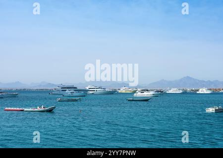 Une vue sereine sur une étendue d'océan bleu parsemée de nombreux bateaux et yachts, contre une chaîne de montagnes lointaine sous un ciel bleu clair Banque D'Images