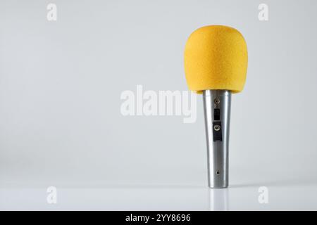 Microphone à main en métal avec pare-brise en mousse jaune sur table blanche avec fond isolé léger. Banque D'Images