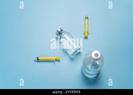 Bouteilles en verre de médicament liquide et seringues en plastique pour l'injection sur le fond bleu. Vue de dessus. Santé et concept médical. Banque D'Images