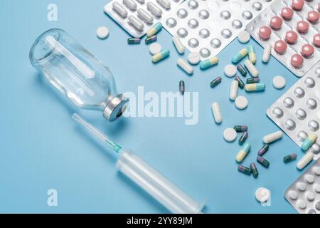 Flacon en verre de médicament liquide, seringue en plastique pour injection et quelques gélules différentes avec plaquettes thermoformées pleines sur le dos bleu Banque D'Images