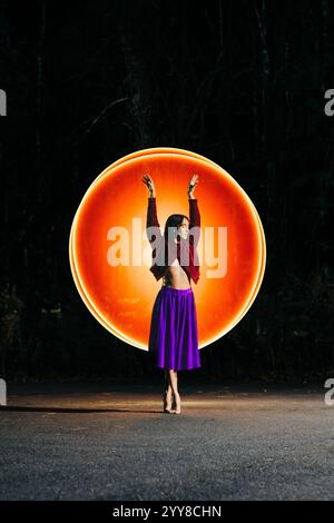 Femme en jupe violette pose devant un cercle de lumière Banque D'Images