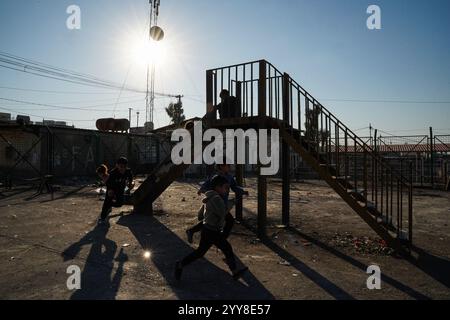 Une vue en silhouette montre des enfants jouer dans une cour au camp de Domiz pour les réfugiés kurdes syriens à environ 18 km au sud-ouest de la ville de Duhok dans la région du Kurdistan. La province de Duhok accueille 92 000 réfugiés syriens sur les 275 000 réfugiés de la région du Kurdistan irakien qui ont migré depuis le déclenchement de la révolution syrienne en 2011. La plupart d’entre eux refusent de retourner dans leur pays malgré la chute du régime de Bachar al-Assad par crainte de l’éclatement de conflits armés entre les Forces démocratiques syriennes (FDS) et l’Armée nationale syrienne soutenue par la Turquie ou avec Hayat Tahrir al-Sham et d’autres opposants Banque D'Images