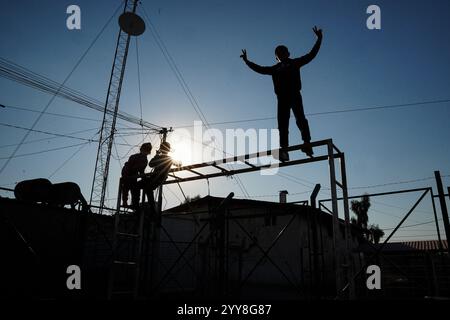 Une vue en silhouette montre des enfants jouer dans une cour au camp de Domiz pour les réfugiés kurdes syriens à environ 18 km au sud-ouest de la ville de Duhok dans la région du Kurdistan. La province de Duhok accueille 92 000 réfugiés syriens sur les 275 000 réfugiés de la région du Kurdistan irakien qui ont migré depuis le déclenchement de la révolution syrienne en 2011. La plupart d’entre eux refusent de retourner dans leur pays malgré la chute du régime de Bachar al-Assad par crainte de l’éclatement de conflits armés entre les Forces démocratiques syriennes (FDS) et l’Armée nationale syrienne soutenue par la Turquie ou avec Hayat Tahrir al-Sham et d’autres opposants Banque D'Images