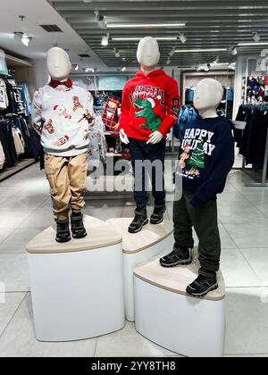 Kiev, Ukraine - 18 décembre 2024 : trois figurines de mannequin de taille enfant exposent des chandails vibrants sur le thème des fêtes dans un magasin de détail moderne. Saison variée Banque D'Images