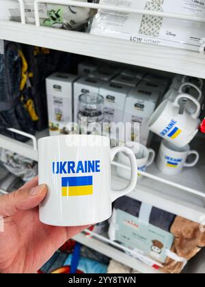 Kiev, Ukraine - 18 décembre 2024 : photo d'une personne tenant une tasse en céramique blanche avec le texte "Ukraine" et le drapeau national, située dans une maison Banque D'Images