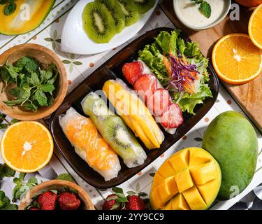 Bonheur tropical sur une assiette ! Ces rouleaux de printemps aux fruits sont une explosion de fraîcheur et de douceur naturelle, avec mangue, kiwi, fraises et enveloppement d'orange Banque D'Images